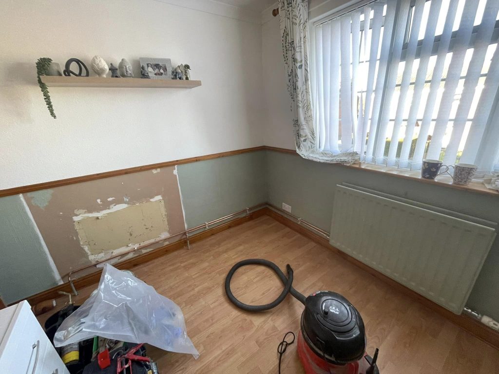 Room with bare wall patch and new radiator installed under the window with visible pipework.