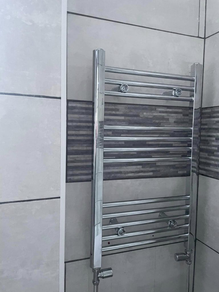 AFTER: Close-up of a new chrome towel rail fitted in a bathroom with grey tiles.